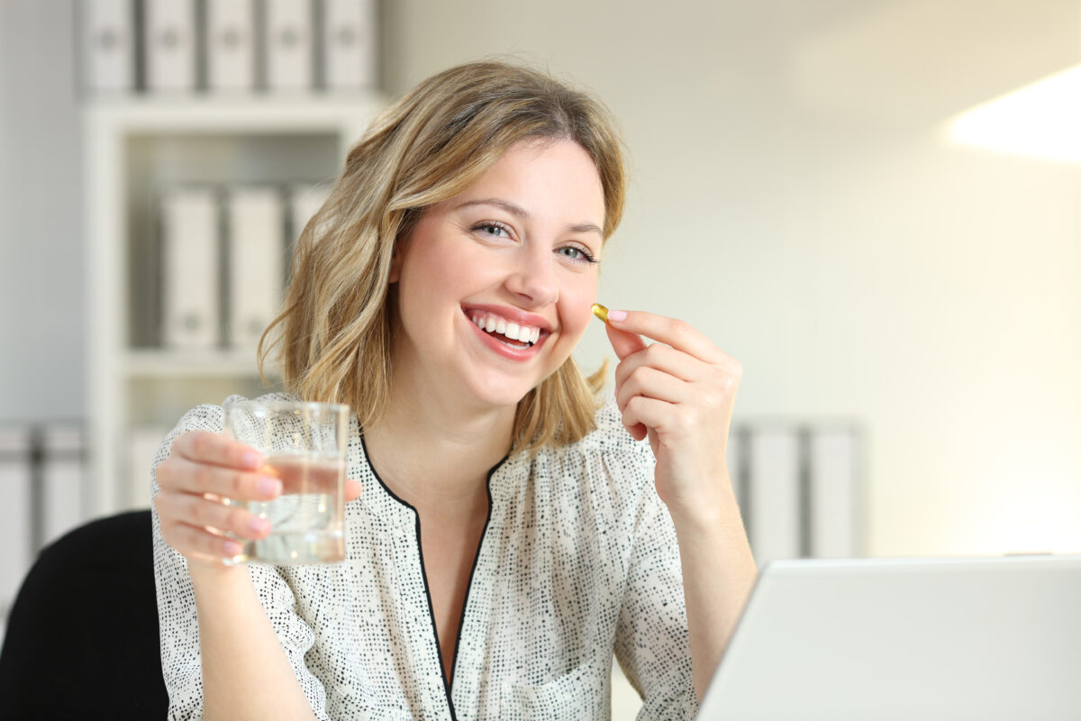 Lucrător de birou fericit care arată o pastilă de supliment de vitamine și un pahar de apă care se uită la camera de luat vederi